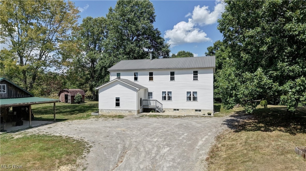 Front view of property with driveway, a metal roof, a lawn, view of scattered trees.