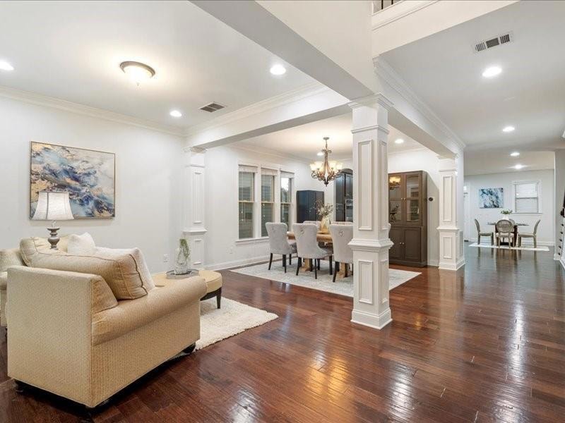 Living area featuring decorative columns, dark wood-style floors, a chandelier, ornamental molding, and recessed lighting