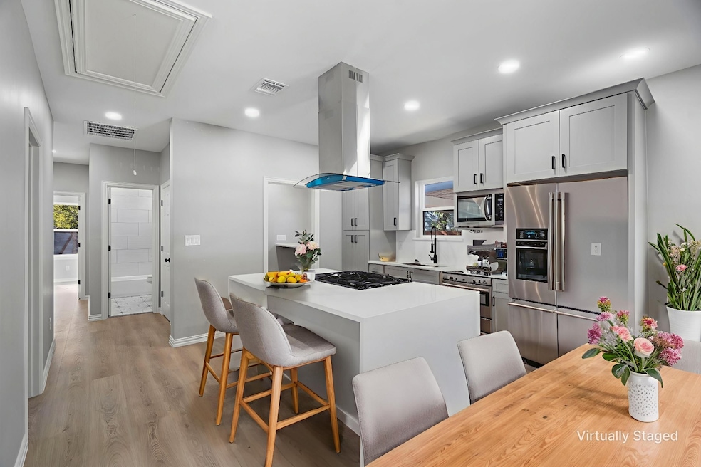 Kitchen with a breakfast bar, appliances with stainless steel finishes, light wood finished floors, recessed lighting, and island range hood