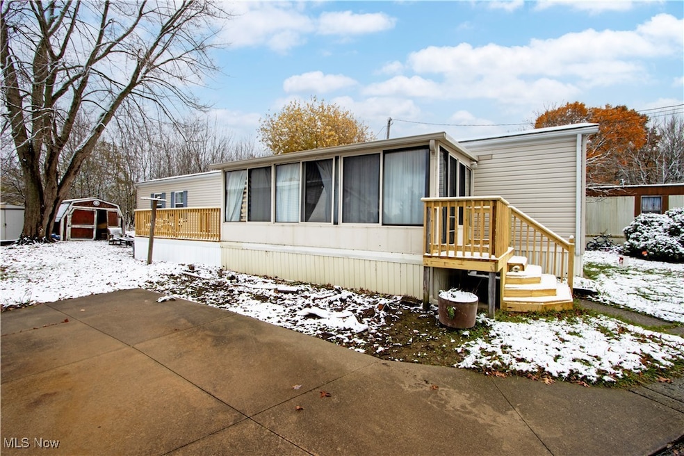 Snow covered house with a sunroom, a wooden deck, and a storage shed