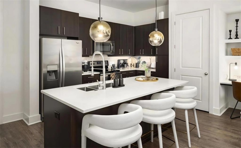 Kitchen featuring dark brown cabinets, a kitchen bar, an island with sink, dark hardwood / wood-style floors, and appliances with stainless steel finishes