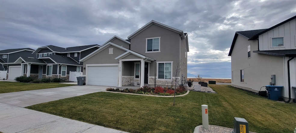 View of front of home featuring concrete driveway, stucco siding, a front lawn, and stone siding