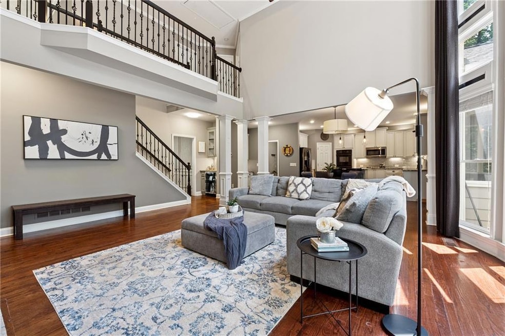 Living area featuring ornate columns, a towering ceiling, stairway, dark wood finished floors, and baseboards