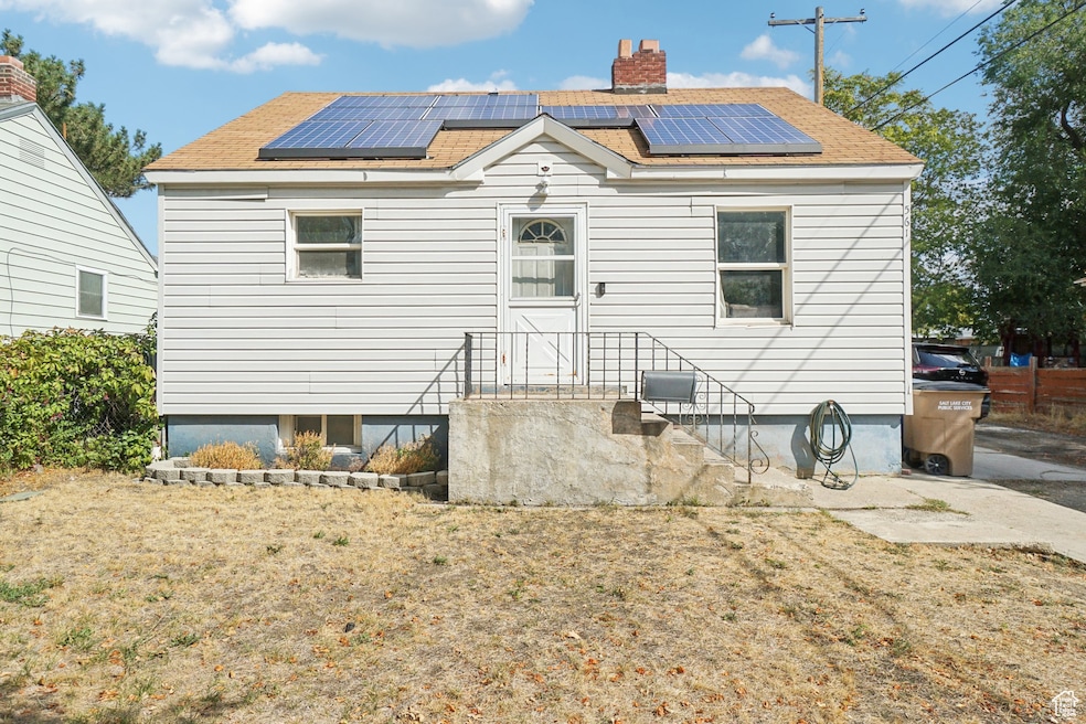 Rear view of property featuring solar panels, a chimney, and a shingled roof