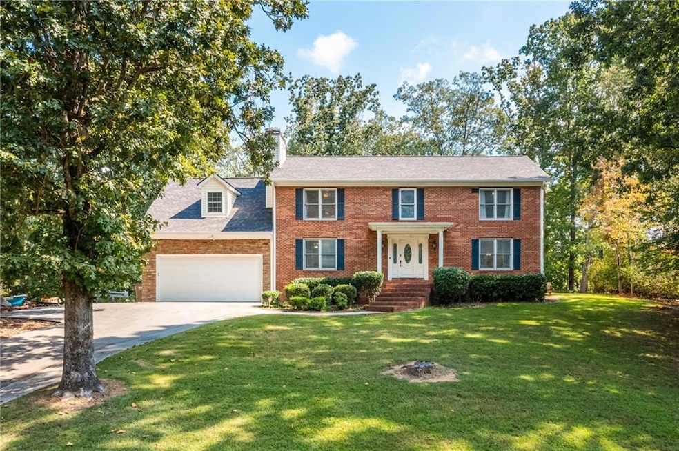 Colonial inspired home featuring a front lawn, driveway, brick siding, an attached garage, and roof with shingles