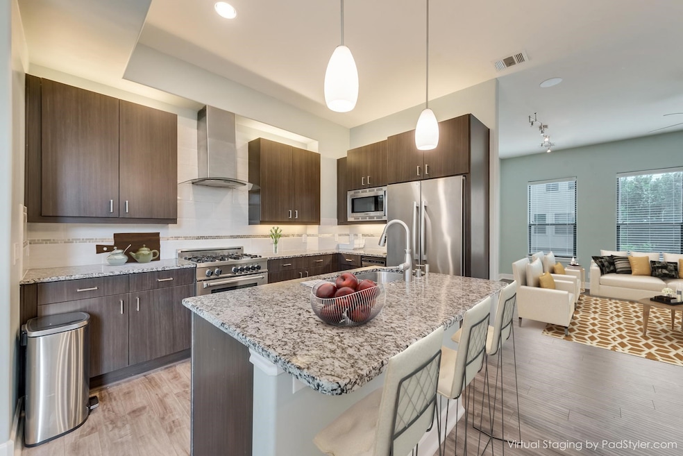 Kitchen with a breakfast bar area, light wood finished floors, wall chimney range hood, decorative light fixtures, and appliances with stainless steel finishes