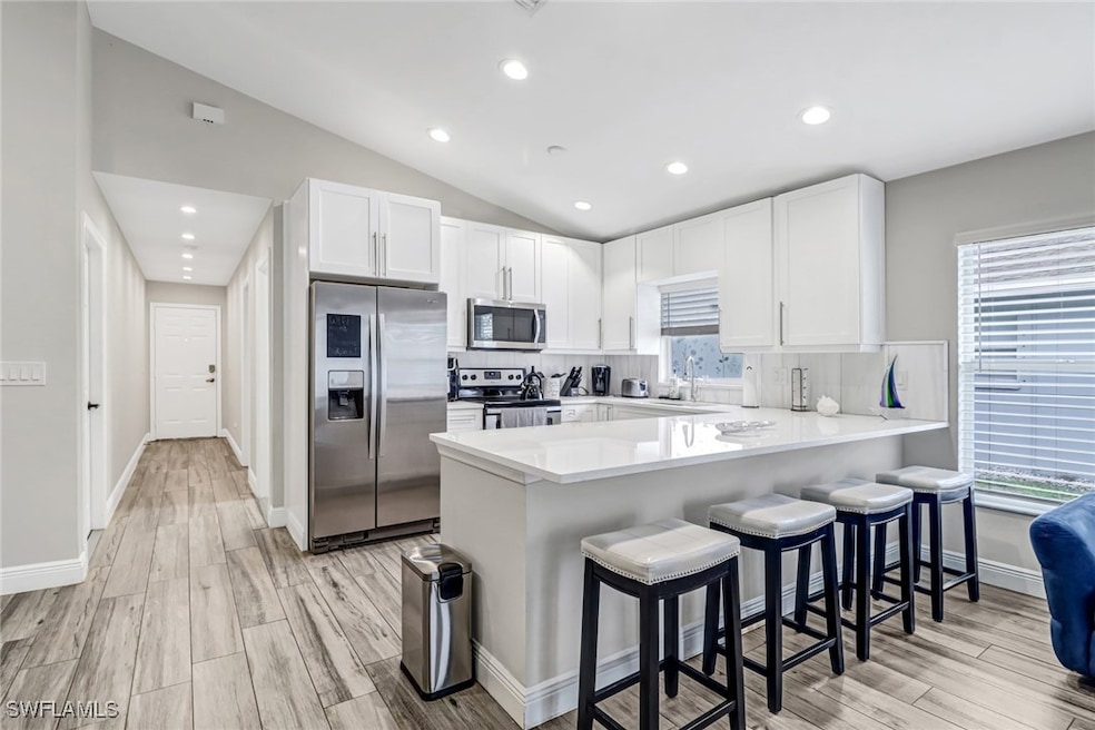 Kitchen featuring stainless steel appliances, a peninsula, white cabinets, light countertops, and a kitchen breakfast bar
