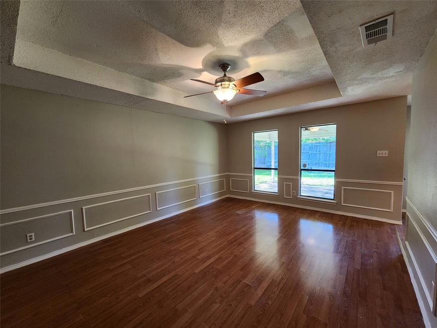 Empty room with ceiling fan, dark wood-type flooring, a raised ceiling, and a textured ceiling