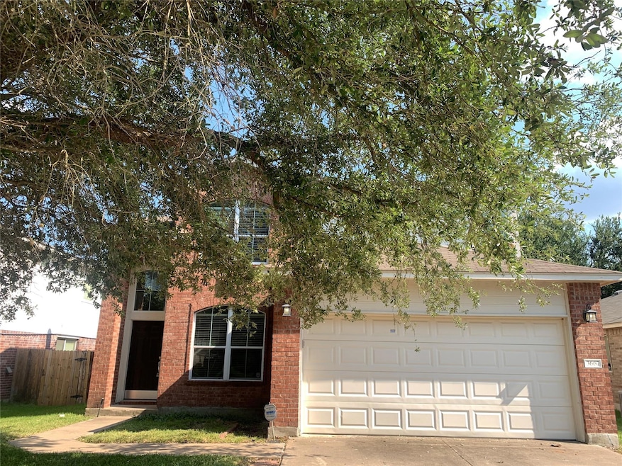 View of property hidden behind natural elements featuring brick siding and concrete driveway