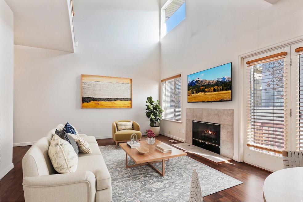 Living room with healthy amount of natural light, a towering ceiling, a fireplace, and wood finished floors