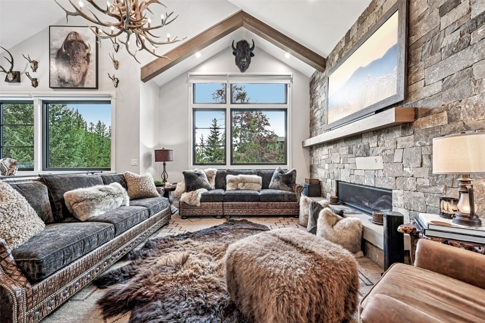 Living room featuring a stone fireplace, high vaulted ceiling, and a chandelier