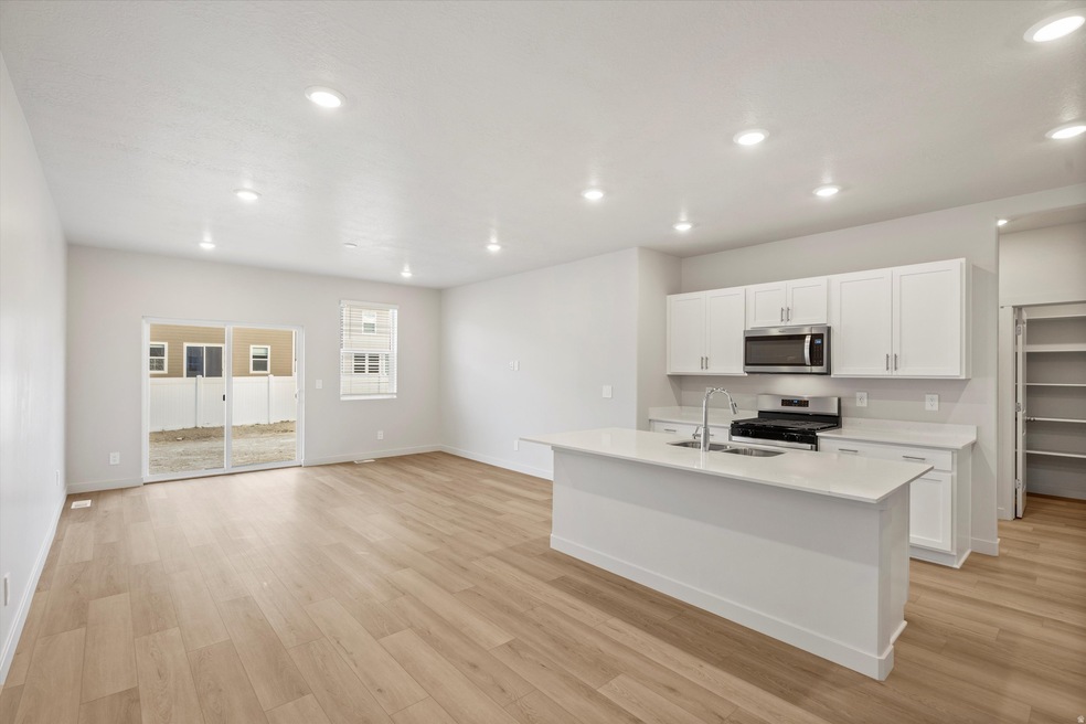 Kitchen with white cabinetry, stainless steel appliances, an island with sink, light wood-style floors, and recessed lighting