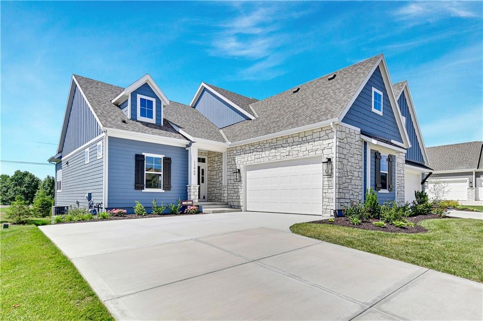 View of front facade with a shingled roof, driveway, stone siding, a garage, and a front yard