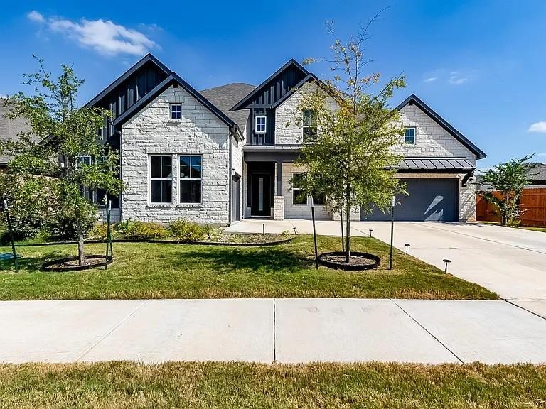 View of front facade with stone siding, concrete driveway, a garage, and a standing seam roof