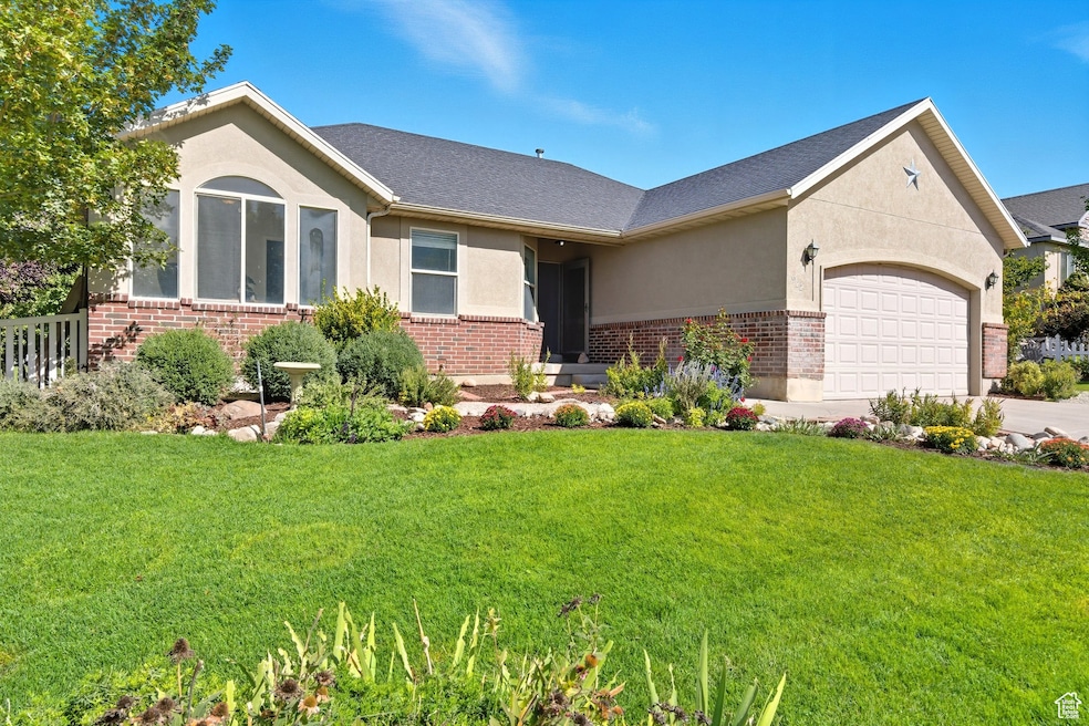 Single story home featuring stucco siding, brick siding, an attached garage, and a front lawn