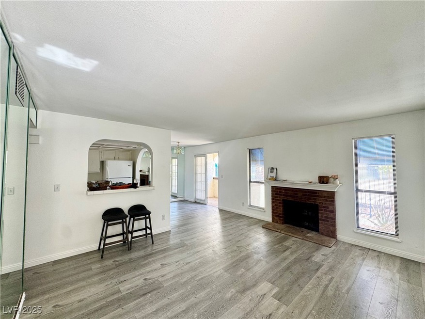 Living area with a textured ceiling, wood finished floors, a brick fireplace, and arched walkways