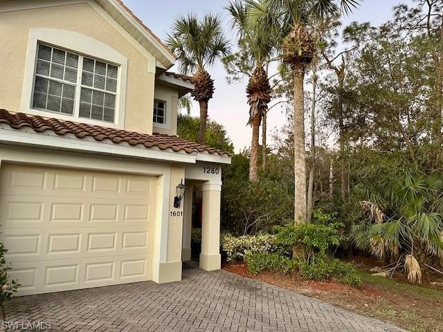 View of front of home with a tiled roof, stucco siding, decorative driveway, and a garage