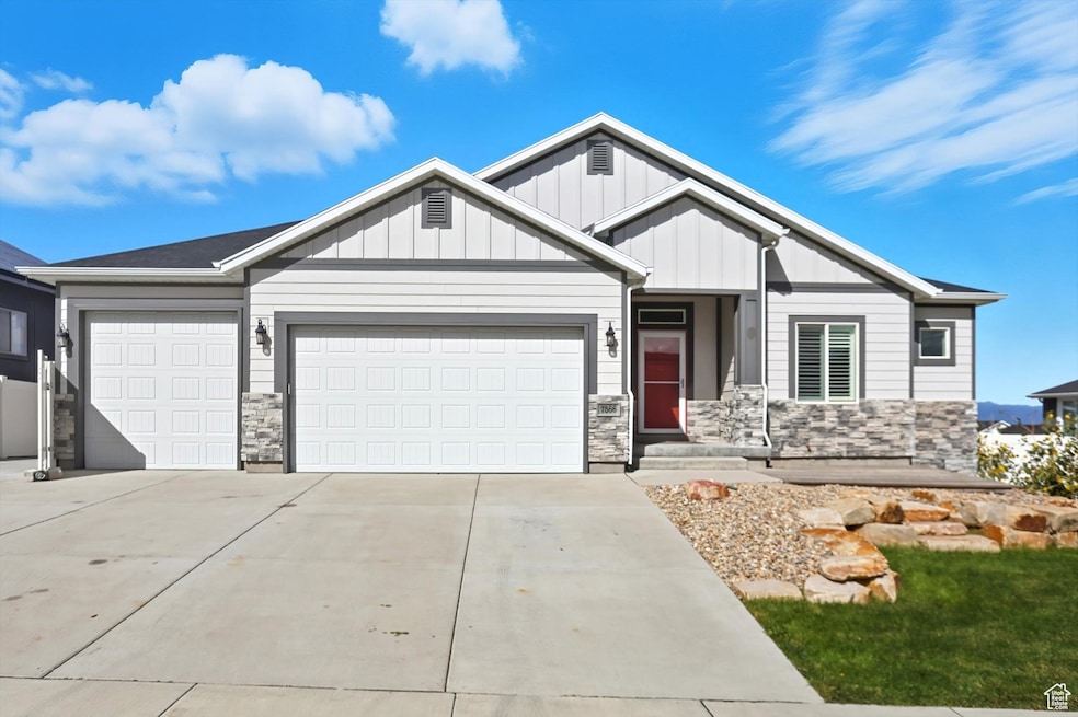 View of front of property with stone siding, board and batten siding, driveway, and an attached garage