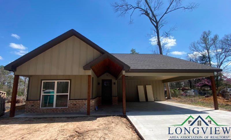View of front of property with brick siding, concrete driveway, board and batten siding, a carport, and roof with shingles