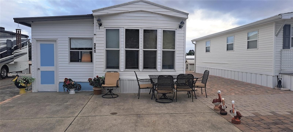 FRONT VIEW W/ NEW DOOR & PAVED DRIVEWAY, PAVED SIDES, AND PAVED REAR PATIO. ON LEFT IS ANOTHER LOT WITH MOTOR HOME (NOT FOR SALE) TO THE RIGHT IS A PARK MODEL (ALSO NOT FOR SALE).