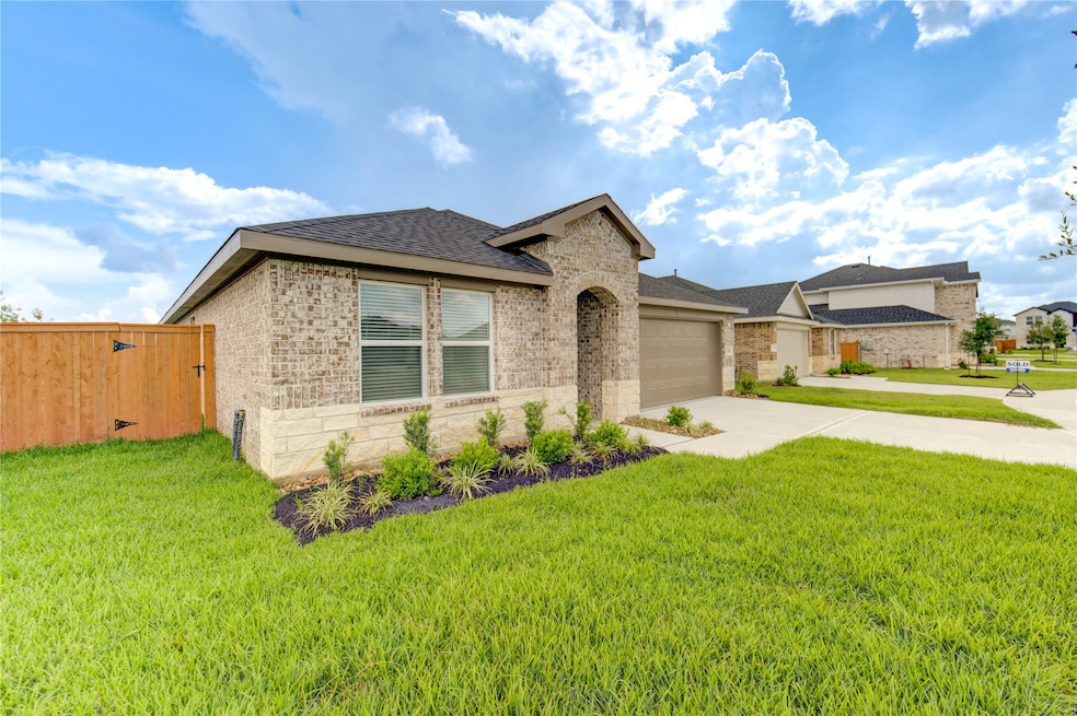 Charming single-story brick home with a neatly landscaped front yard, modern windows, and a spacious driveway leading to a two-car garage. The property is fenced with a wooden gate for added privacy.