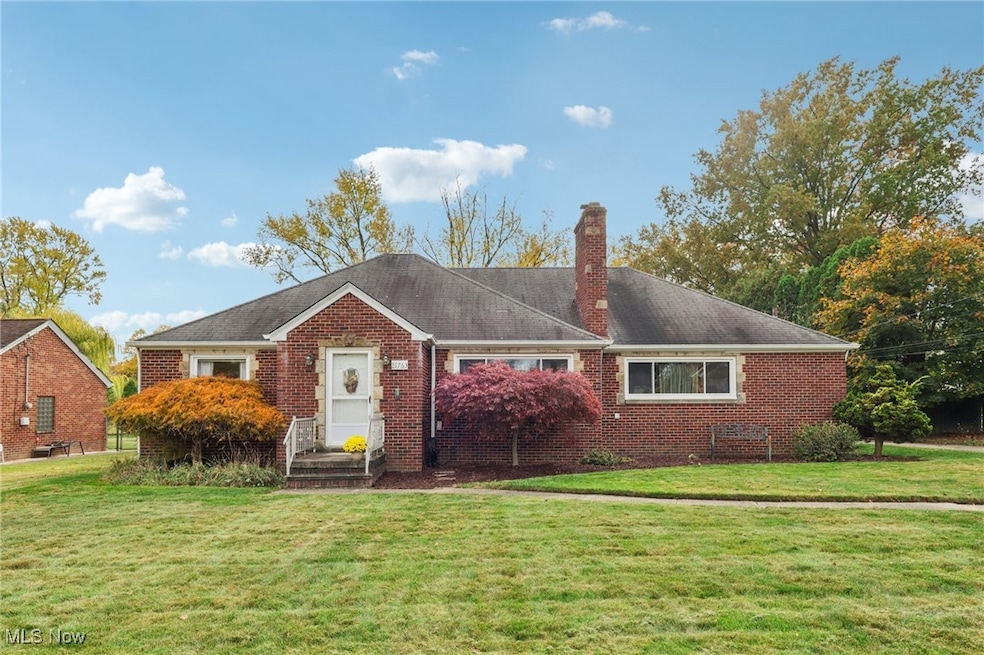 View of front facade featuring a front lawn, a chimney, brick siding, and roof with shingles