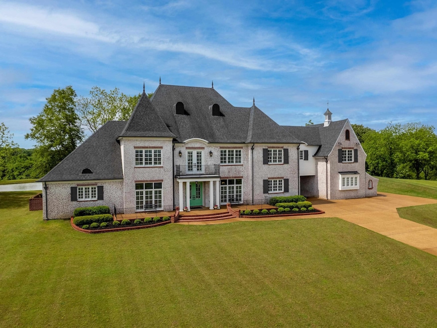 French country style house featuring a balcony, a front lawn, concrete driveway, and brick siding