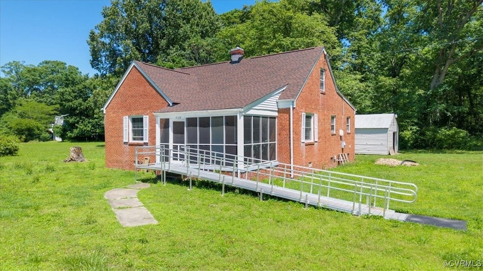 Back of property featuring a sunroom, a lawn, bric