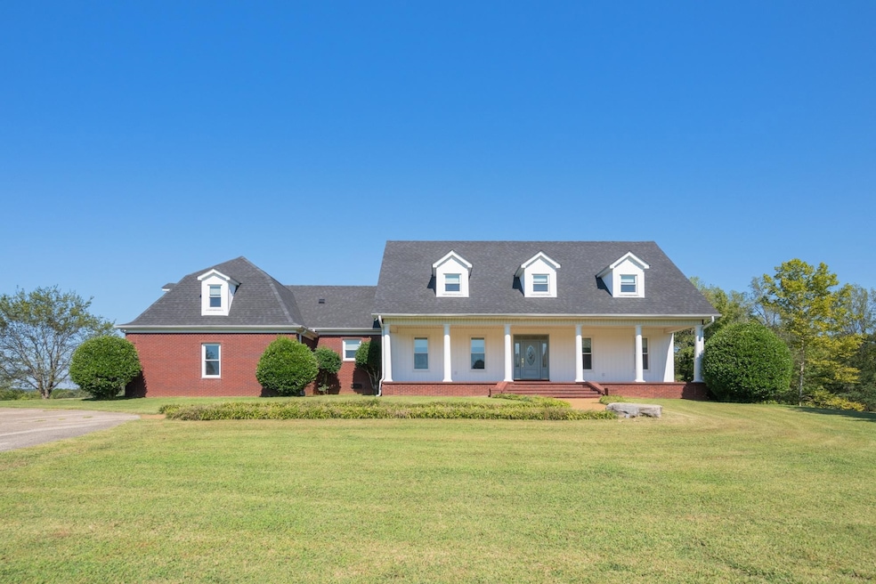 Cape cod house with a front yard, brick siding, covered porch, and a shingled roof