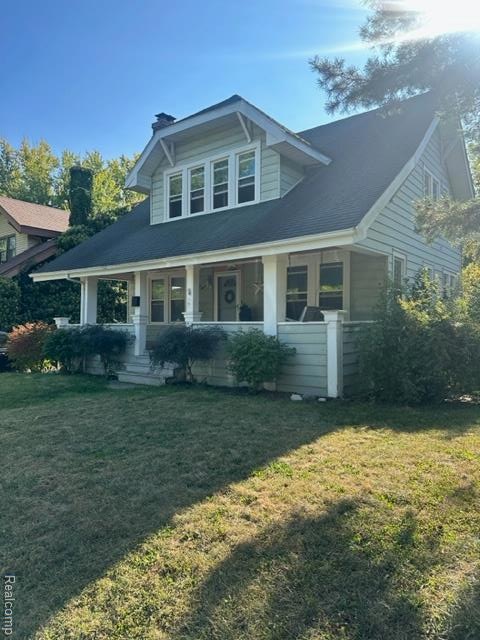 View of front of property featuring a porch, a chimney, a front lawn, and a shingled roof