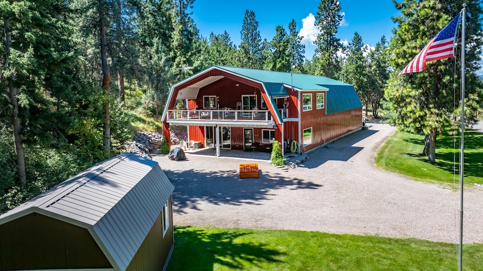 View of front of property with a gambrel roof, a metal roof, a deck, and gravel driveway