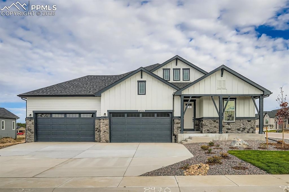 View of front of home with stone siding, covered porch, board and batten siding, driveway, and roof with shingles