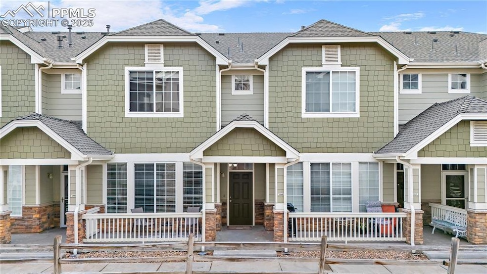 Townhome / multi-family property with covered porch, stone siding, and a shingled roof
