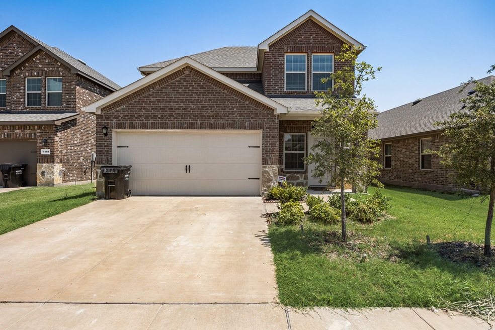 View of front of home with a front yard, roof with shingles, brick siding, driveway, and a garage