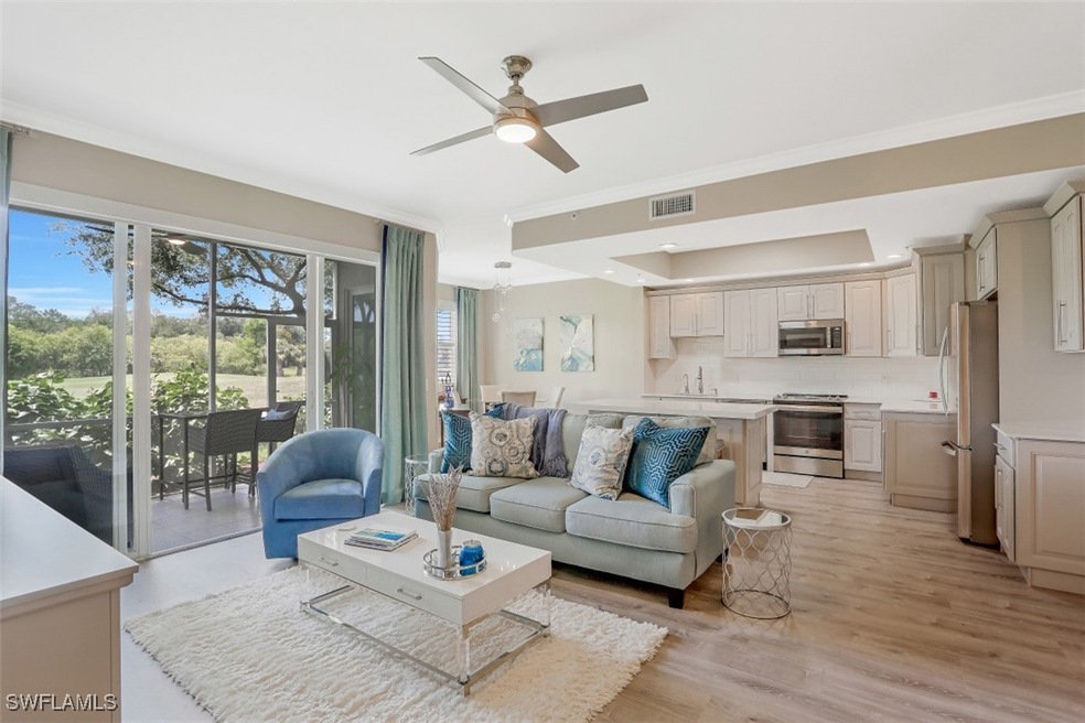 Living area featuring a ceiling fan, ornamental molding, light wood finished floors, and a tray ceiling