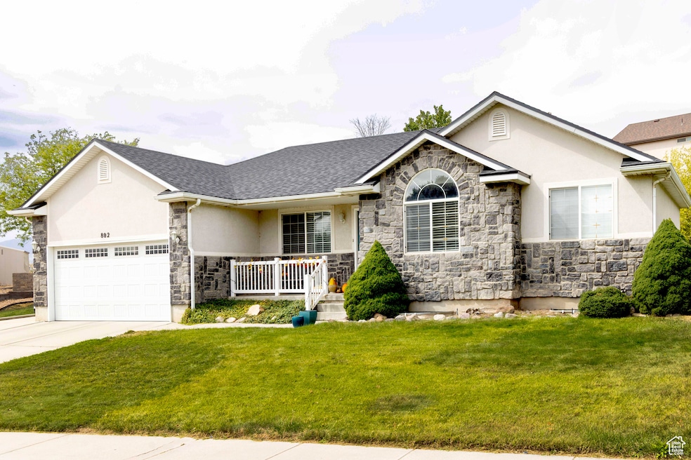 View of front of home with stone siding, a front yard, stucco siding, and a garage