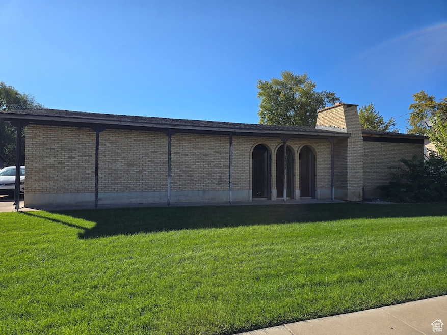 Rear view of house featuring brick siding, a lawn, a chimney, and a patio