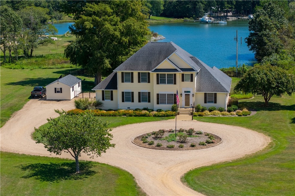 View of front of property with curved driveway, a shingled roof, a water view, a front yard, and stucco siding