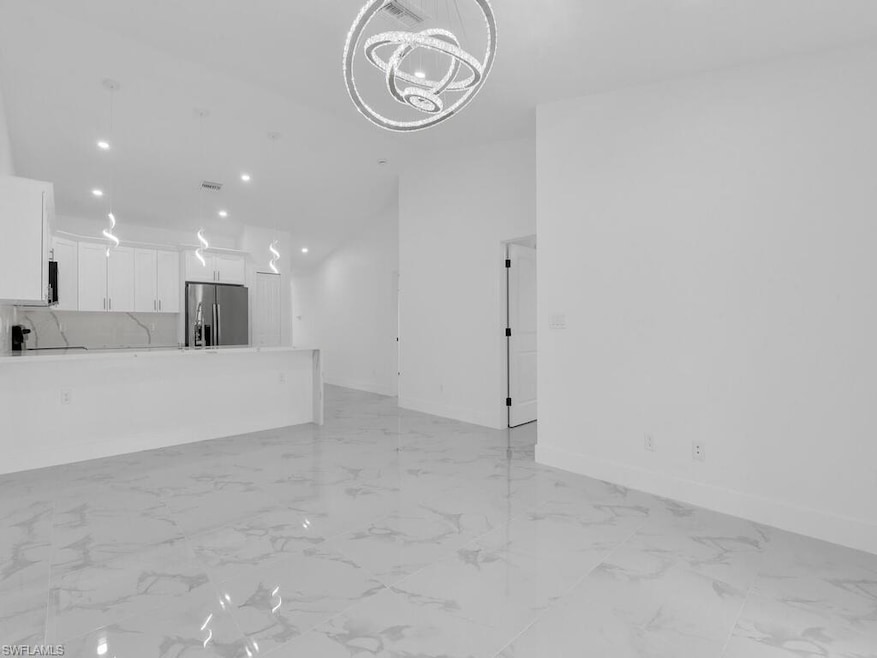 Unfurnished living room featuring a chandelier, light marble finish flooring, and baseboards