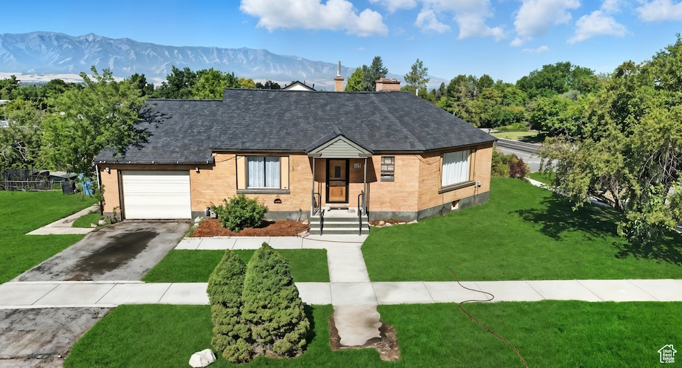 View of front of house featuring driveway, roof with shingles, a mountain view, brick siding, and a chimney *This image has been digitally enhanced.