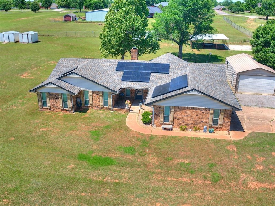 View of front of home with an outdoor structure, brick siding, a chimney, a shingled roof, and roof mounted solar panels