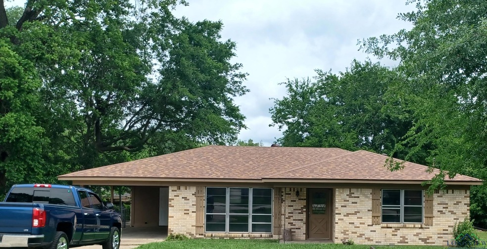 Single story home featuring brick siding, a shingled roof, an attached carport, and a front yard