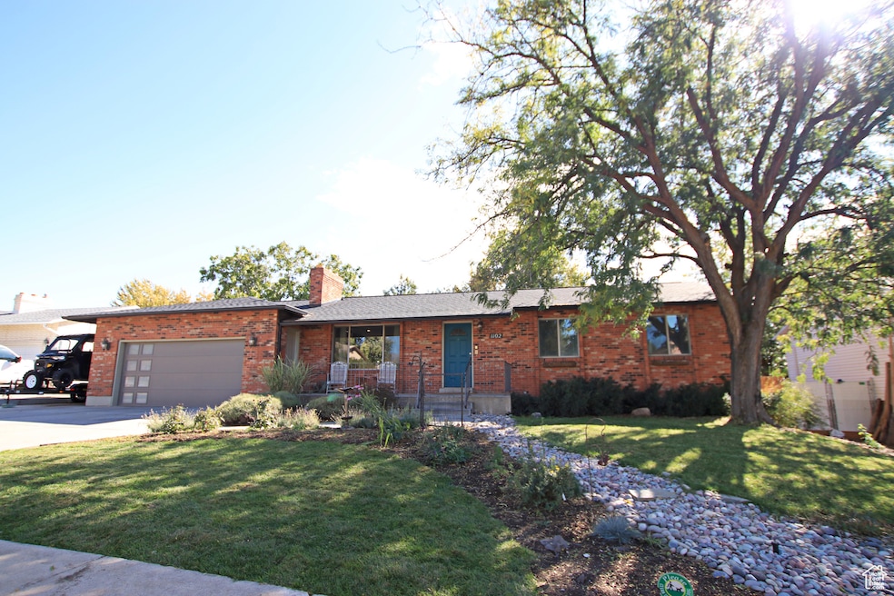Single story home featuring brick siding, a front lawn, driveway, a chimney, and a garage