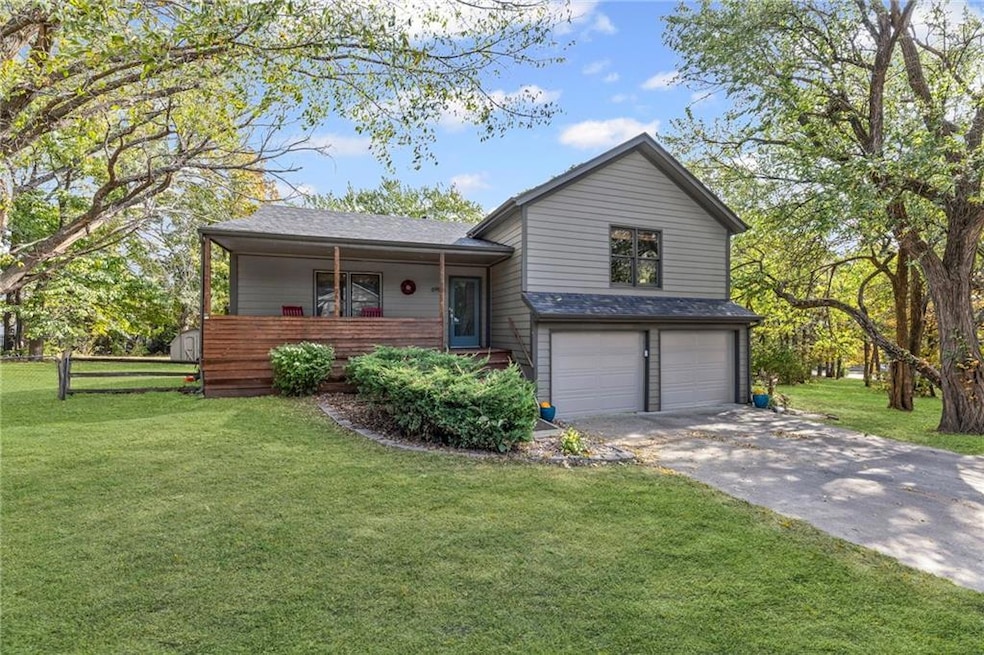 Split level home with a front lawn, driveway, an attached garage, roof with shingles, and a porch