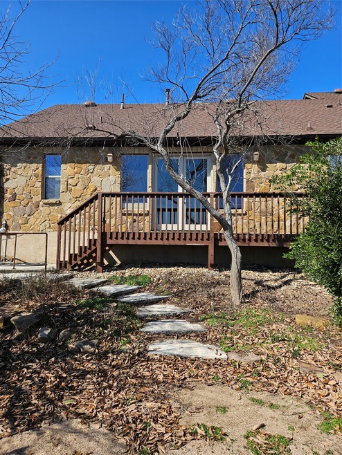 Rear view of house with stone siding, roof with shingles, and a wooden deck