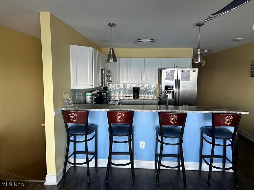 Kitchen with stainless steel appliances, a peninsula, backsplash, and decorative light fixtures