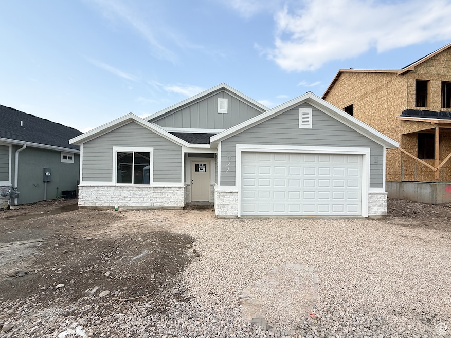 View of front facade with board and batten siding, stone siding, driveway, and an attached garage