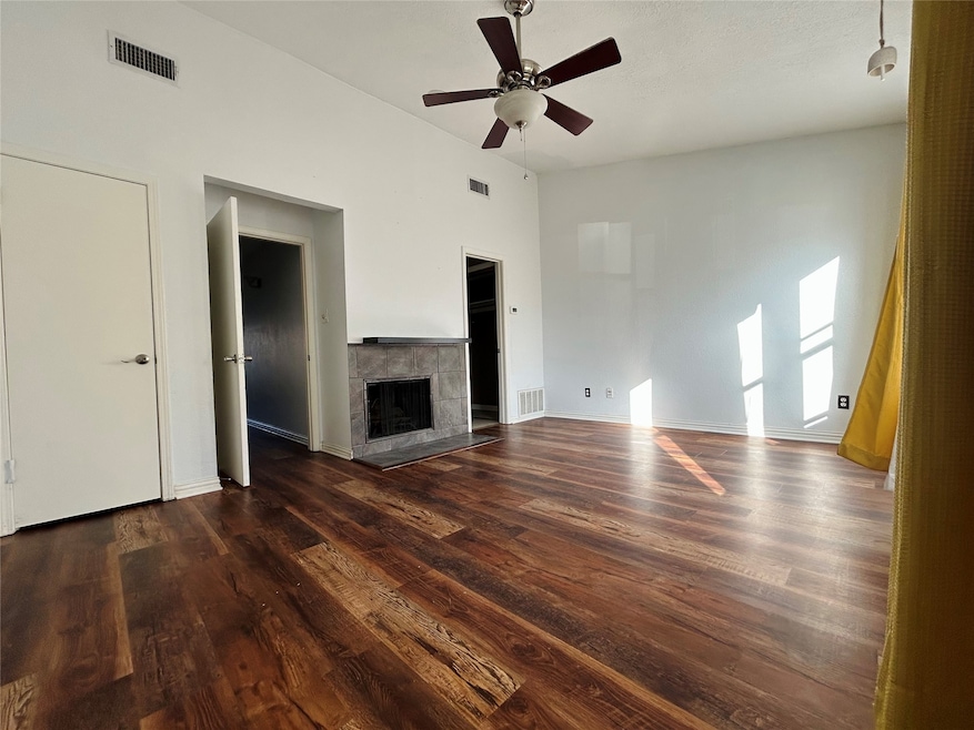 Unfurnished living room featuring dark wood-style flooring, a tile fireplace, and a ceiling fan
