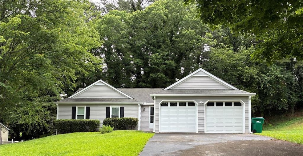 View of front of home with a front lawn, driveway, a garage, view of wooded area, and roof with shingles