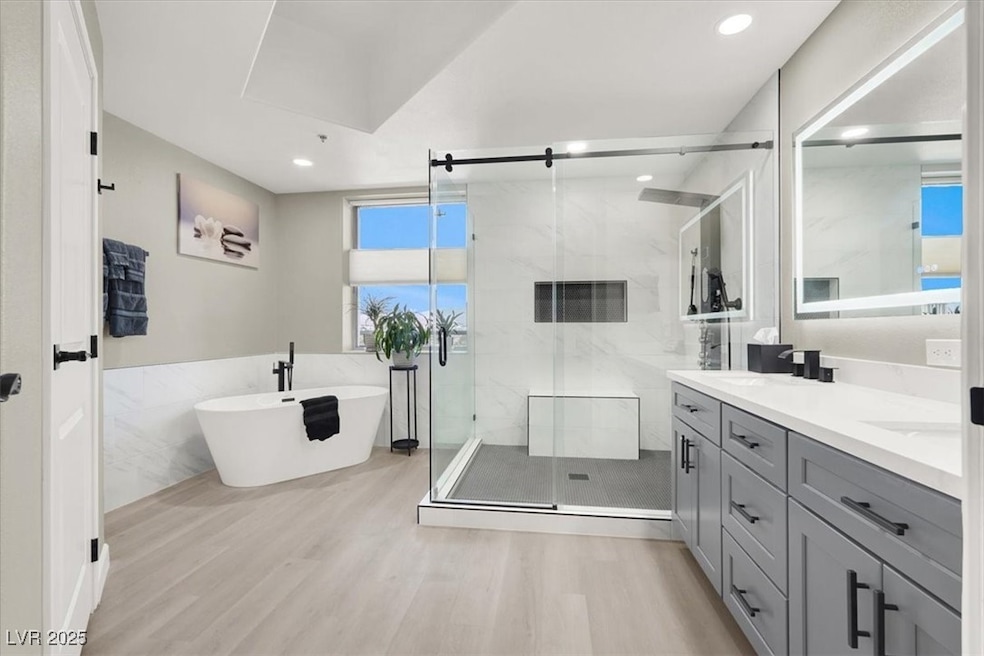 Bathroom with double vanity, wood finished floors, a soaking tub, a marble finish shower, and recessed lighting